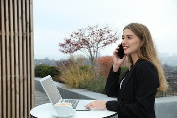 Businesswoman with laptop talking on phone in outdoor cafe. Corporate blog