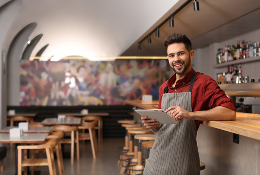 Young male business owner with tablet near counter in his cafe. Space for text