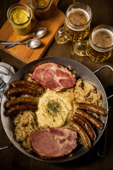 Sauerkraut Pfanne mit Nürnberger Rostbratwürste, Kassler Nacken,  Kartoffelpüree Senf und Bier auf Holz Tisch