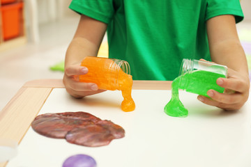 Little boy pouring slime onto table indoors, closeup