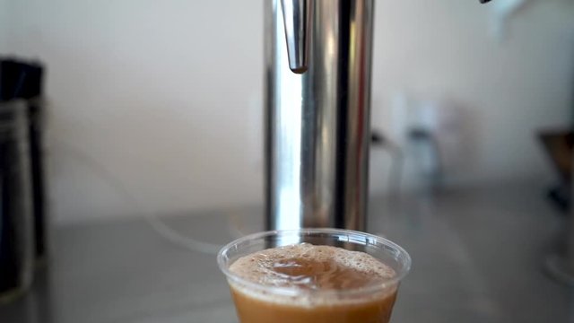 Pouring nitro cold brew coffee from a cold brew coffee tap into a plastic cup in a cafe.