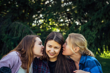 Fototapeta premium Portrait of three young girlfriends who whisper in the park. Exchange of news, emotional women whispering gossip.