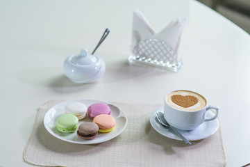 Fototapeta na wymiar Delicious cappuccino and macaroons prepared on a table for a guest