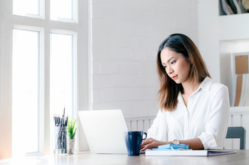 Portrait of young businesswoman looking at laptop screen while sitting at office desk in modern office.