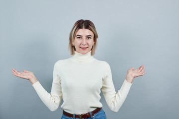 Shocked cheerful young woman in white sweater, looking camera, spreading hands isolated on gray...