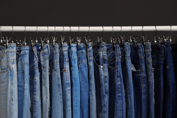 Rack with different jeans on dark grey background