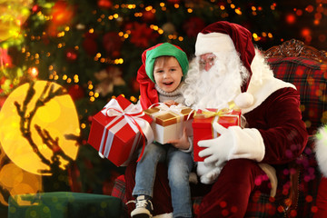 Fototapeta na wymiar Santa Claus and little boy with gifts near Christmas tree indoors