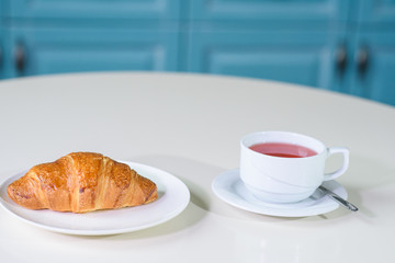 Fruit tea and delicious fresh croissant on the table in a cozy coffee shop