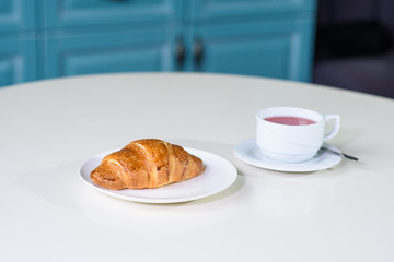 Fruit tea and delicious fresh croissant on the table in a cozy coffee shop