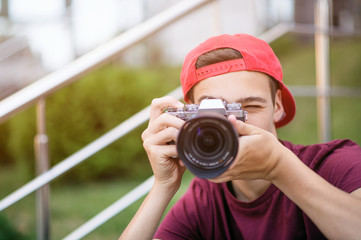 Teenage boy taking photos outdoors. Young man works reporter, outdoors. Caucasian guy holds a photo...