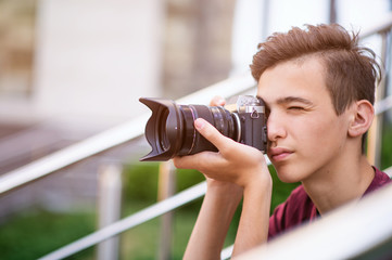 Teenage boy taking photos outdoors. Young man works reporter, outdoors. Caucasian guy holds a photo...