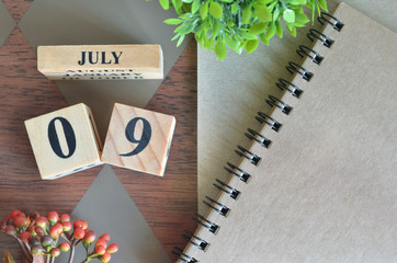 July 9. Date of July month. Number Cube with a flower and notebook on Diamond wood table for the 