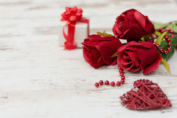 Red roses, gift box and wooden decorated hear on white wooden background.