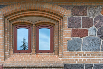 Window in the wall of rubble masonry. The sky and the tree are reflected in the glass.