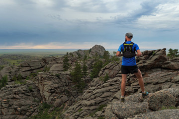 Male runner standing on the edge of a mountain cliff and looking at the vast valley.