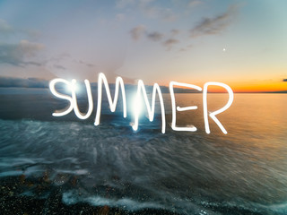 Summer letters made with flashlight or light pen over sea castline in sunset light. Live composite...