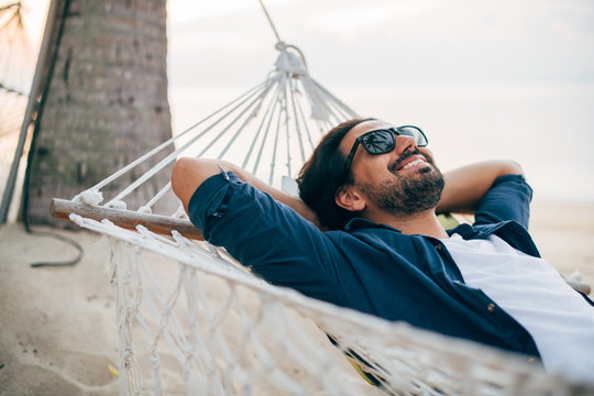 A man enjoys calm, lies in a hammock on the background of the ocean and sunset.
