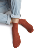 Cropped shot of a man's foots in blue jeans, lying on a white background. It is terracotta socks on his foots. 
