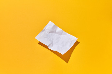 Crumpled paper sheet with hard shadows on an yellow background.
