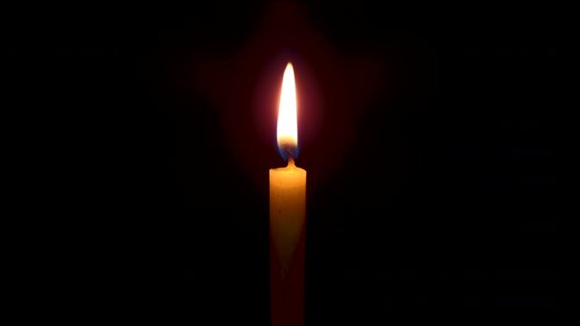 The flame from an orange candle has a black background.