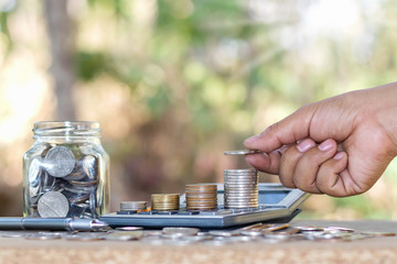 Woman's hand holding a coin and stacking coins on a financial concept calculator and saving money.