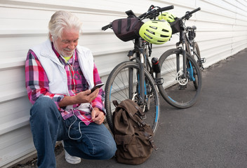 senior man with earphones against a white metal wall. Listening some music at his mobile phone....