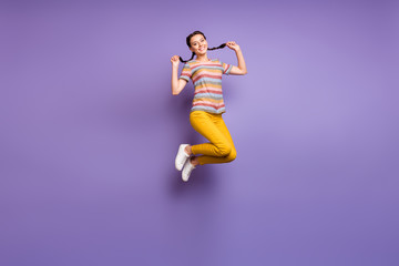Full length photo of crazy lady jumping high in amazing summer mood holding pretty braids wear casual striped t-shirt yellow pants isolated purple color background