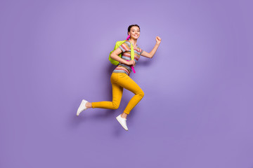 Full body profile photo of funky lady jumping high carry school bag rushing home lessons finish wear casual striped t-shirt yellow trousers isolated purple color background