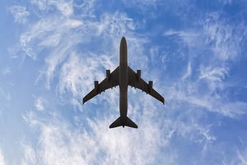 Bottom view of a plane with two turbines that flies against a blue sky with a cloud