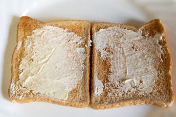 Top view of 2 pieces of white toast with butter spread on them isolated on white plate. Breakfast, snack. Toasted bread.