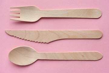 Eco cutlery from pine wood. Disposable tableware from natural materials. Wooden spoon, fork and knife agains a pink background. Zero waste, plastic free, stop pollution concept.