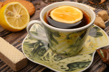 A Cup of black tea, sliced lemon, brown sugar slices, oatmeal cookies, waffles on a wooden background. Close up.