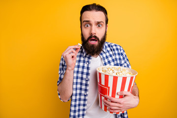 Portrait of nice attractive worried scared addicted bearded guy in checked shirt overeating popcorn junk snack watching scary video isolated over bright vivid shine vibrant yellow color background