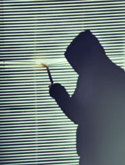 Criminal with crowbar is spying through the window. Old shutter blinds.