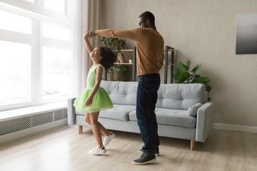 Black dad dance with happy daughter in green dress