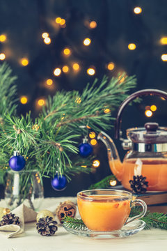 Christmas and New Year composition. Cup and teapot of hot spicy tea with sea buckthorn, jam in the glass jar, branches of pine and spruce, holiday decor, bokeh, dark background