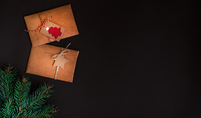 Christmas border on dark background, composed of fresh fir branches and envelope of kraft paper. Merry Christmas and Happy Holidays! Flat lay, top view, copy space.
