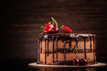Chocolate cake with with berries, strawberries and cherries. cake on a dark brown background. copy...