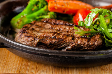 American food concept. Grilled beef steak with grilled vegetables, with carrots, cherry tomatoes, broccoli, in a cast iron pan. copy space
