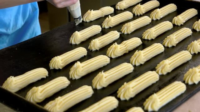 Eclairs extruded from pastry bag. The tray with eclair dough ready for cook. How to make classic french eclairs at home.