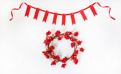 Christmas composition. Garland made of red small flags and red satin ribbon with wreath of red berries on pastel background. Christmas, winter, new year concept. Flat lay, top view, copy space.