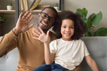 Smiling black dad and daughter wave talking on webcam