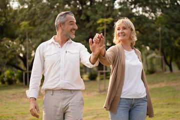 Senior elegant caucasian couple dancing looking at each other feeling love and cherish on their anniversary in the park with copy space, happily retired spouse, well-managed retirement life concept.