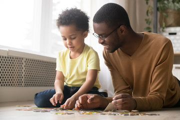 Black dad and little son assemble jigsaw puzzle together