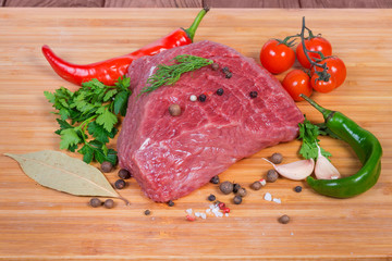 Piece of uncooked beef among vegetables, greens and spices