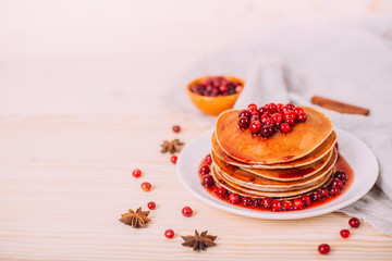Stack of american pancakes with fresh cranberry and jam in white plate on wooden rustic table. Delicious dessert for breakfast in winter.
