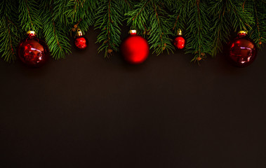 Christmas card concept with fir tree branches and red shiny balls on dark background - text space. Merry Christmas and Happy Holidays greeting card. Flat lay, top view. Copy space for your text.