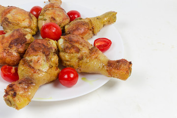 Grilled chicken legs with cherry tomatoes on dish, fragment closeup