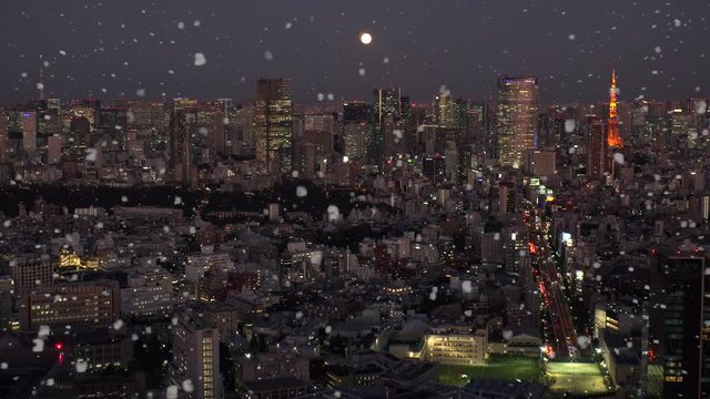 TOKYO, JAPAN - DECEMBER 2019 : Aerial view of cityscape of TOKYO snowing at night. Scenery of central downtown area. Soft snow falling and full moon in the sky. Winter and Christmas season concept.