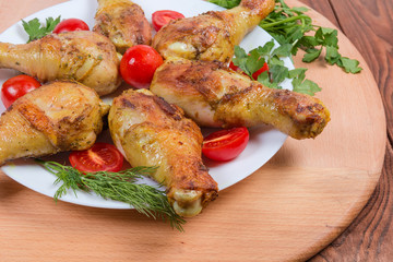 Grilled chicken legs, tomatoes, greens on dish on serving board